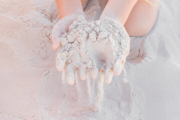 The hands of a young girl hold a pile of white sand close-up © Andrey