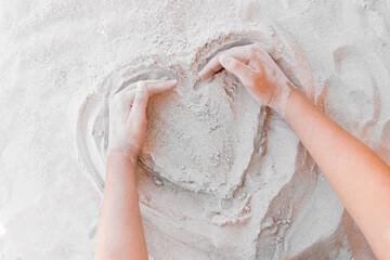 Fototapeta premium The hand of a young girl draws a heart on the white beach sand close-up. Symbol or sign of love concept