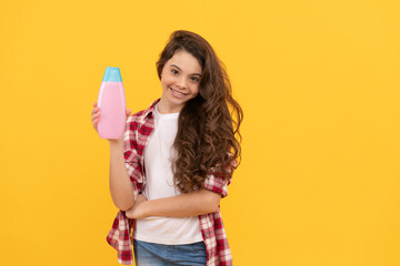 happy teen girl with long curly hair hold shampoo bottle, haircare