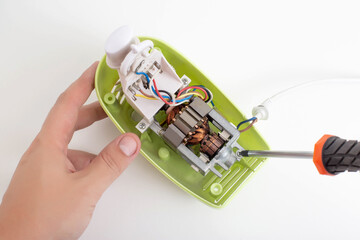 The hands of a male household appliance repairman unscrew the parts of a hand mixer with a...