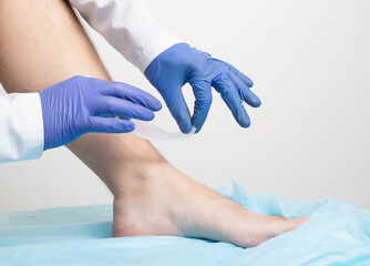 The doctor removes wax strips from the hair of the patient's legs on a white background. Leg hair removal concept, close-up