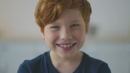 Close up portrait of happy adorable little redhead boy with freckles smiling and posing to camera