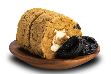 Closeup view of sliced prune sponge cake roll with pittrd dried prune in wooden plate on white background.