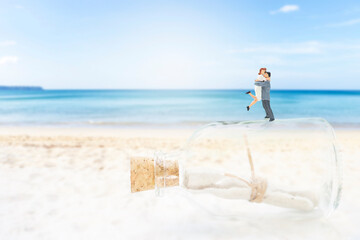 Miniature couple on glass bottle over blurred beach background, love message, valentine concept background, outdoor day light, love letter