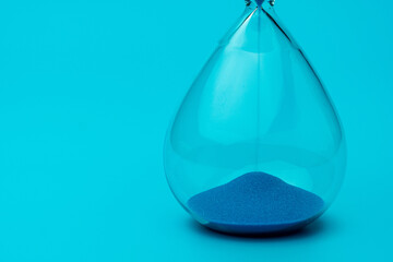 Hourglass with blue sand on blue background