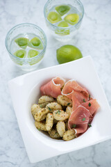 Potato gnocchi with green basil pesto and prosciutto on a light-grey marble background, vertical shot, elevated view