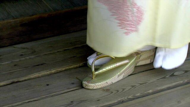 Close-up of Japanese woman's feet as she removes sandals and places them on the Getabako shoe cupboard.