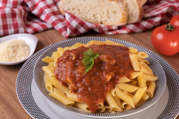 macarrão com molho de tomate servido dentro do prato ao lado de fatias de pão italiano e toalha xadrez