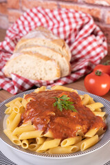 macarrão com molho de tomate servido dentro do prato ao lado de fatias de pão italiano e toalha...