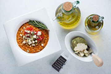 Top view of risotto with sun dried tomato pesto and belper knolle over white stone background, horizontal shot