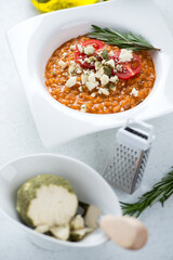 Plate of italian risotto with red pesto sauce and belper knolle cheese, vertical shot on a white stone surface