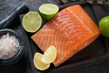 Close-up of raw fresh salmon fillet with lemon, lime and pink salt on a black wooden serving tray, studio shot
