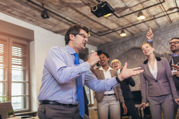 Obraz premium Business people having a karaoke party at the office, singing, dancing and having fun while taking a break from a bussy work day