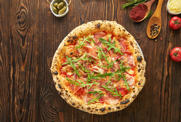 Original italian neapolitan pizza with parma ham and fresh arugula on wooden background with ingredients. Fast food menu eating concept, top view