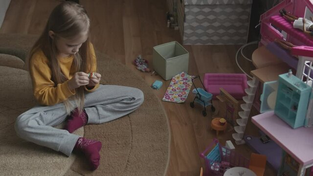 Little six years girl playing in her room with a dolls near dollhouse. Little cute girl sitting on floor and play with dolls. Happy childhood concept.