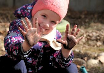 Small girl smiling and showing dirty hands outdoors in garden, sustainable lifestyle concept.