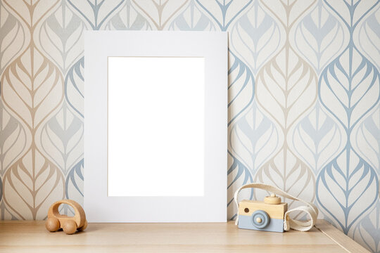 White frame mock up for photo, print art, text or lettering, with kids room decorations and toys. Blank frame on wooden table.