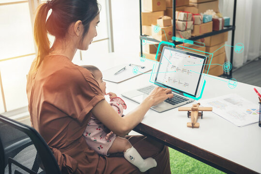 Asia Mother Shopping Online With A Laptop Holding Her Baby Daughter At Home Office. Serious Single Mom With Child. Asian Woman Working From Home, While In Quarantine Isolation During Covid-19 Crisis.