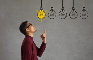 Side profile view young man making choice looking up at several electric light bulbs. Creative Afro...