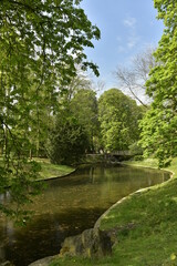 Fototapeta na wymiar L'un des étangs et le pont rustique en rocaille à son bout sous la végétation luxuriante du parc Josaphat à Schaerbeek 