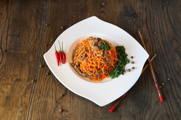 Carrot Korean meat salad with chopsticks on wooden oak table