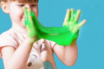 A little girl holds and stretches in her hands a green slime on a blue background. A child is playing with a slippery, sticky toy. Chewing gum in children's hands. Entertainment for children.