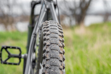 A mountain bike with a dirty studded tire stands against a background of green grass. Rear view. Selective focus