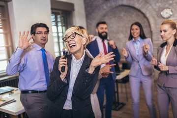 Business people having karaoke party at co-working space, singing, dancing and having fun while taking a break