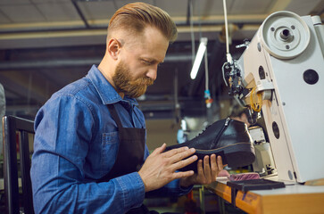 Male worker checking quality of footwear. Side view of man sitting at table with shoe sewing...