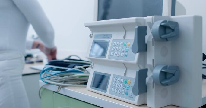 Close-up a multichannel syringe pump device is standing on the table while a female medical worker hand is taking an electric cable to connect it.