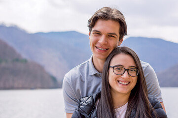 Smiling young couple standing near a lake looking to camera,close up.
