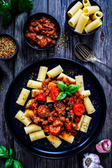 Rigatoni with delicious stew  - aubergine with tomatoes and black olives on wooden table
