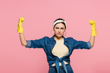 Young housewife in rubber gloves showing muscles isolated on pink