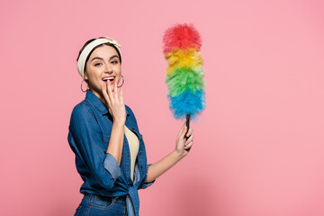 Excited woman in denim shirt holding dust brush on pink background