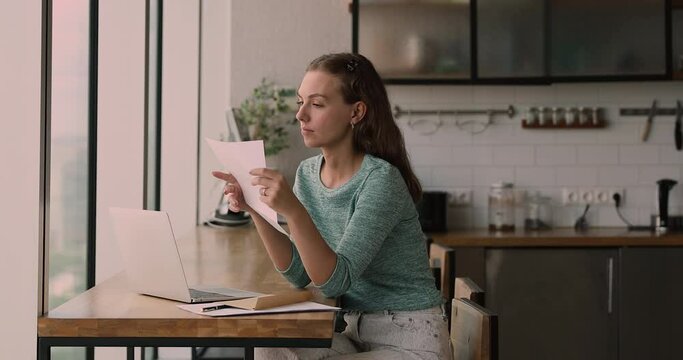 Young woman sit in kitchen at table open envelope smile read letter with pleasant good news, bank loan approved, salary growth, invitation on event, taxes refund, university admission notice concept