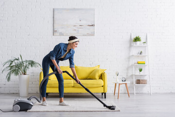 Young woman smiling and cleaning carpet with vacuum cleaner