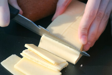 Hands of woman are slicing cutting cheese on nature using knife, preparing cooking food in camping....