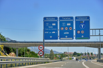 Light traffic in the toll plaza under the blue sky with multiple highway signs, electronic toll...