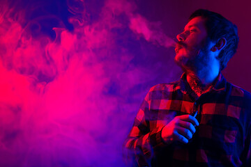Man with tattoos using electronic cigarette and exhaling steam. boy vaping between colored lights...