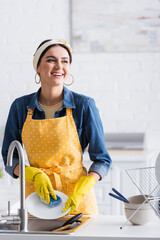 Cheerful woman washing utensil near kitchen sink