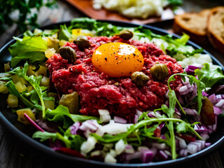 Perfect beef tartare steak with onion, capers, pickled cucumbers and mushrooms on wooden table
