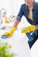 Cropped view of smiling woman cleaning kitchen worktop with detergent and sponge