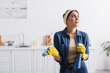 Disappointed housewife in rubber gloves holding sponge and detergent