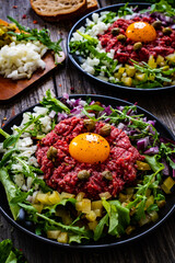 Perfect beef tartare steak with onion, capers, pickled cucumbers and mushrooms on wooden table
