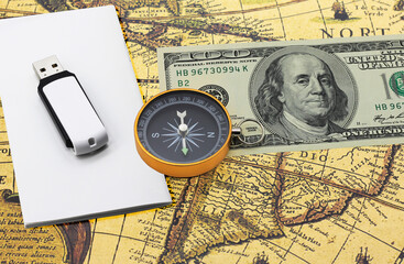 Classic navigation compass on American dollars flash drive on white paper on old vintage world map as symbol of tourism with compass, travel with compass and outdoor activities with compass