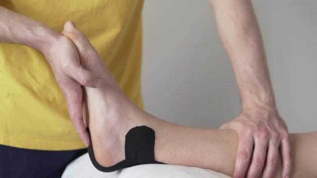 Stretching the Achilles tendon of an athlete after an injury, a rehabilitator does gymnastics for an ankle athlete in a tailpa, close-up.