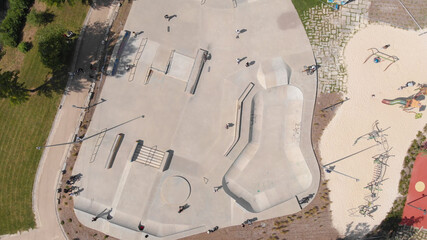 AERIAL DRONE VIEW - Amazing aerial view of the skate park in Santo Tirso city in Portugal with many skaters and bmx bikers on it. The Geao Urban Park with high school building in background. - obrazy, fototapety, plakaty