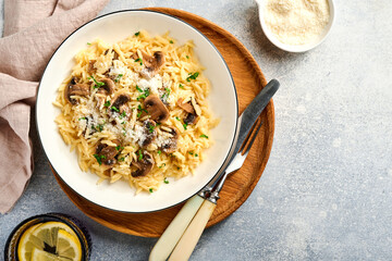 Dining italian pasta risoni, mushrooms, sauce, Parmesan, thyme, garlic, olive oil, in white plate over slate, stone or concrete background. Top view with copy space. Italian cuisine.