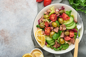 Tuna salad with fresh vegetables, olives, capers and lemon served in bowl on light grey background. Top view with copy space.