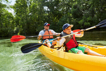 Boy with father in life jacket canoeing with oar in lake during picnic